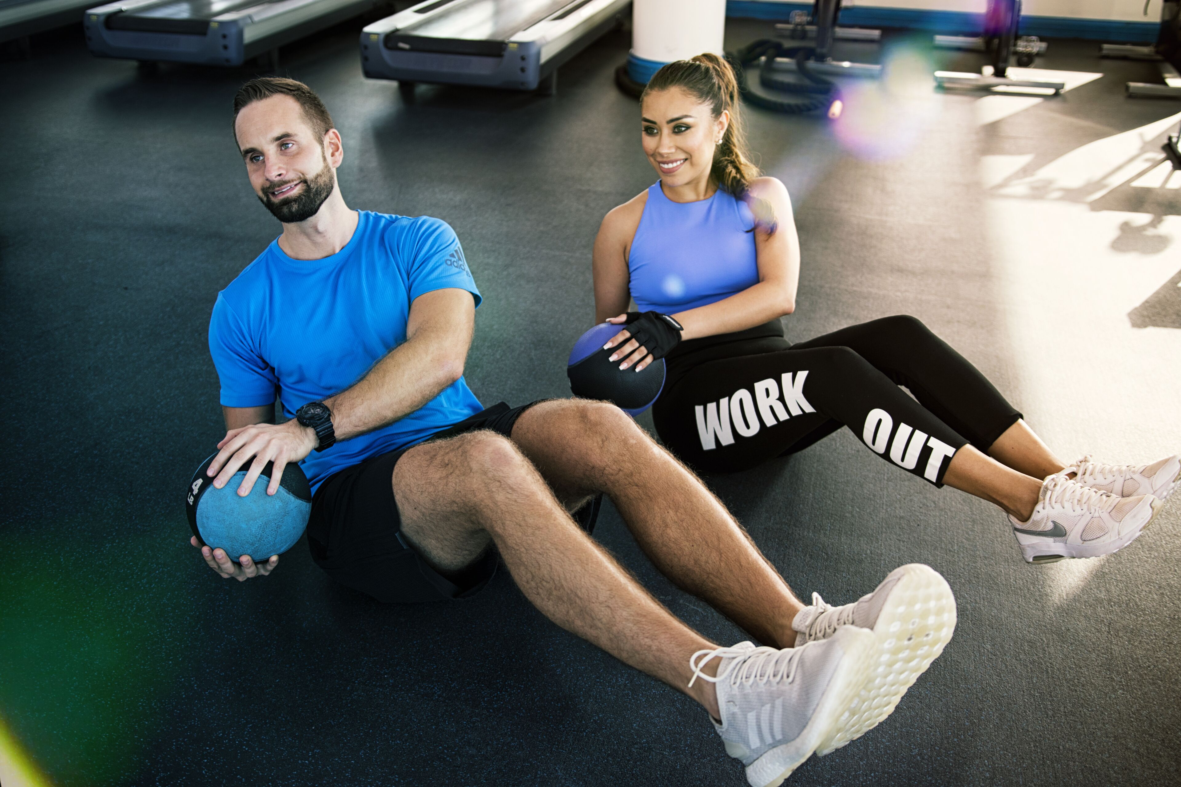 Two people exercising with exercise balls in a gym with treadmills and other fitness equipment.