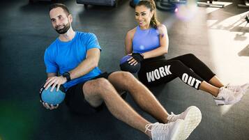 Duas pessoas se exercitando com bolas de ginástica em academia, com esteiras e outros equipamentos de fitness.