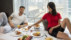 A breakfast setting with a city view, including a table with plates of food, a bowl of fruit, and a glass of orange juice. - Towers Rotana (Dubai)