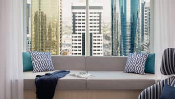 A modern living room with a built-in bench, a view of tall buildings, and a pair of striped armchairs.
