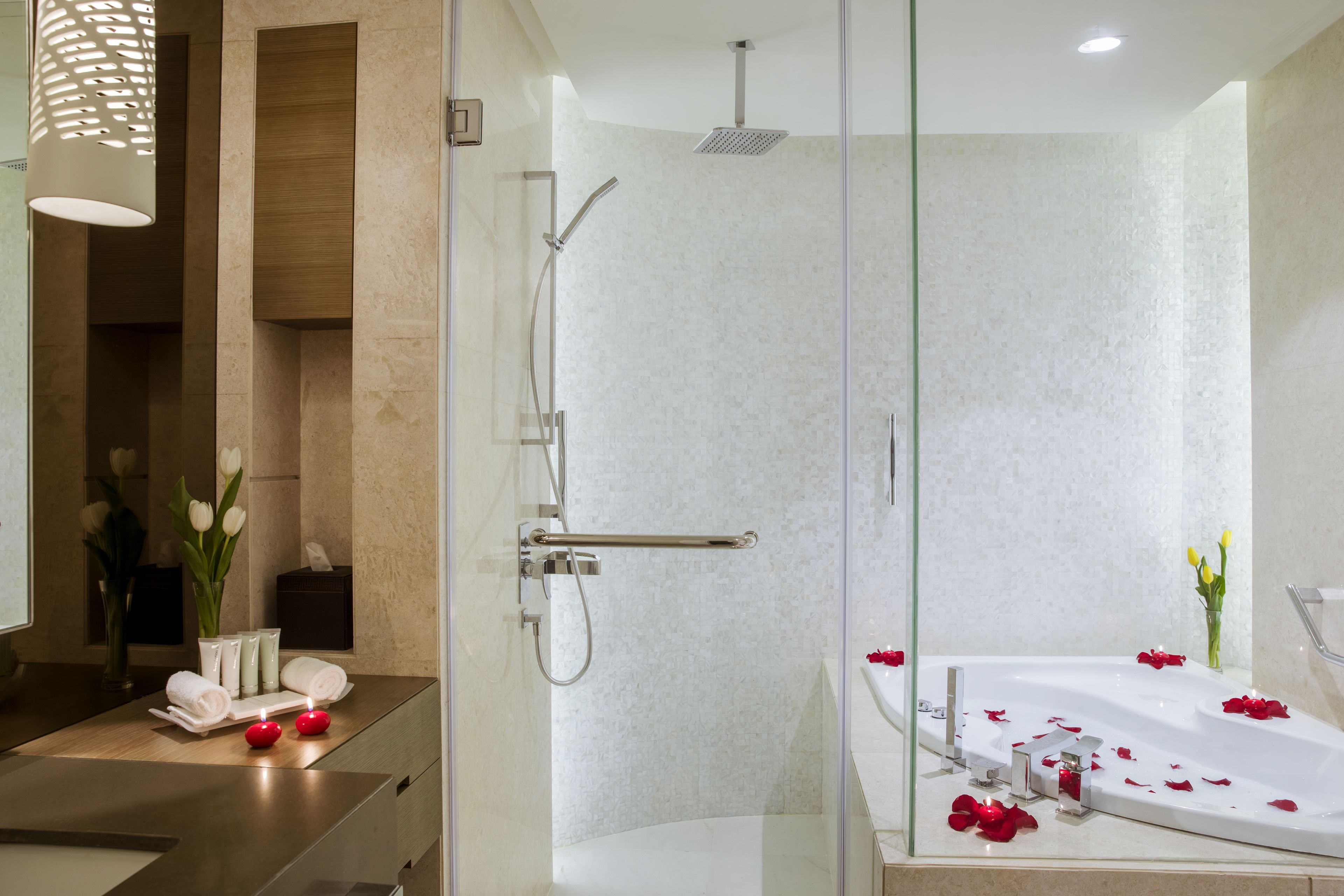 A modern bathroom with a glass-enclosed shower, a separate bathtub with rose petals, and a vanity with toiletries.