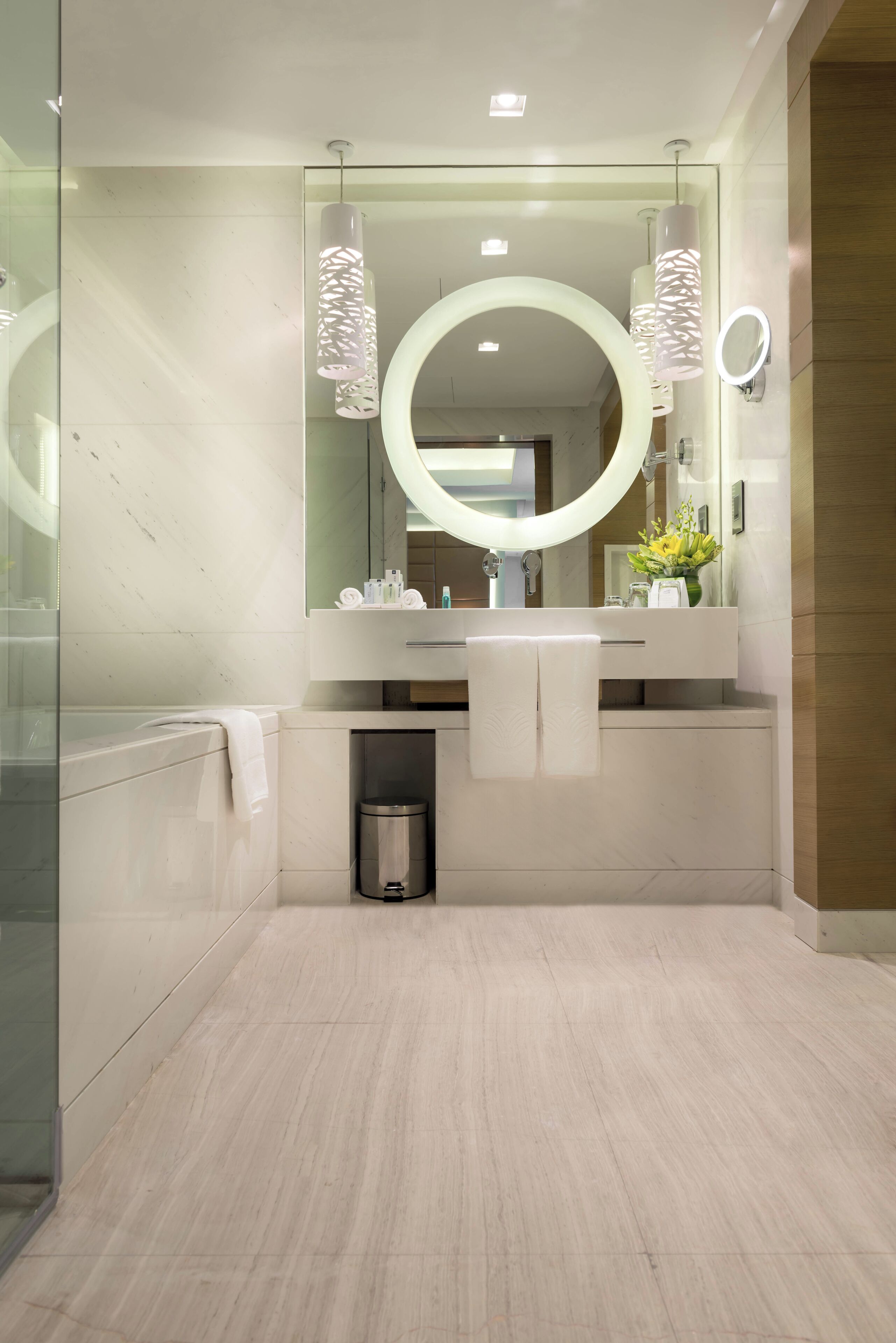 Une salle de bain moderne avec un grand miroir, deux lampes suspendues et un miroir rond fixé au mur.