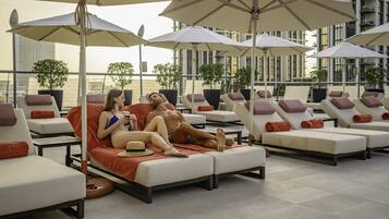Un espace de détente sur le toit, avec des chaises longues et des parasols, offrant une vue sur le paysage urbain et un bâtiment moderne en arrière-plan.