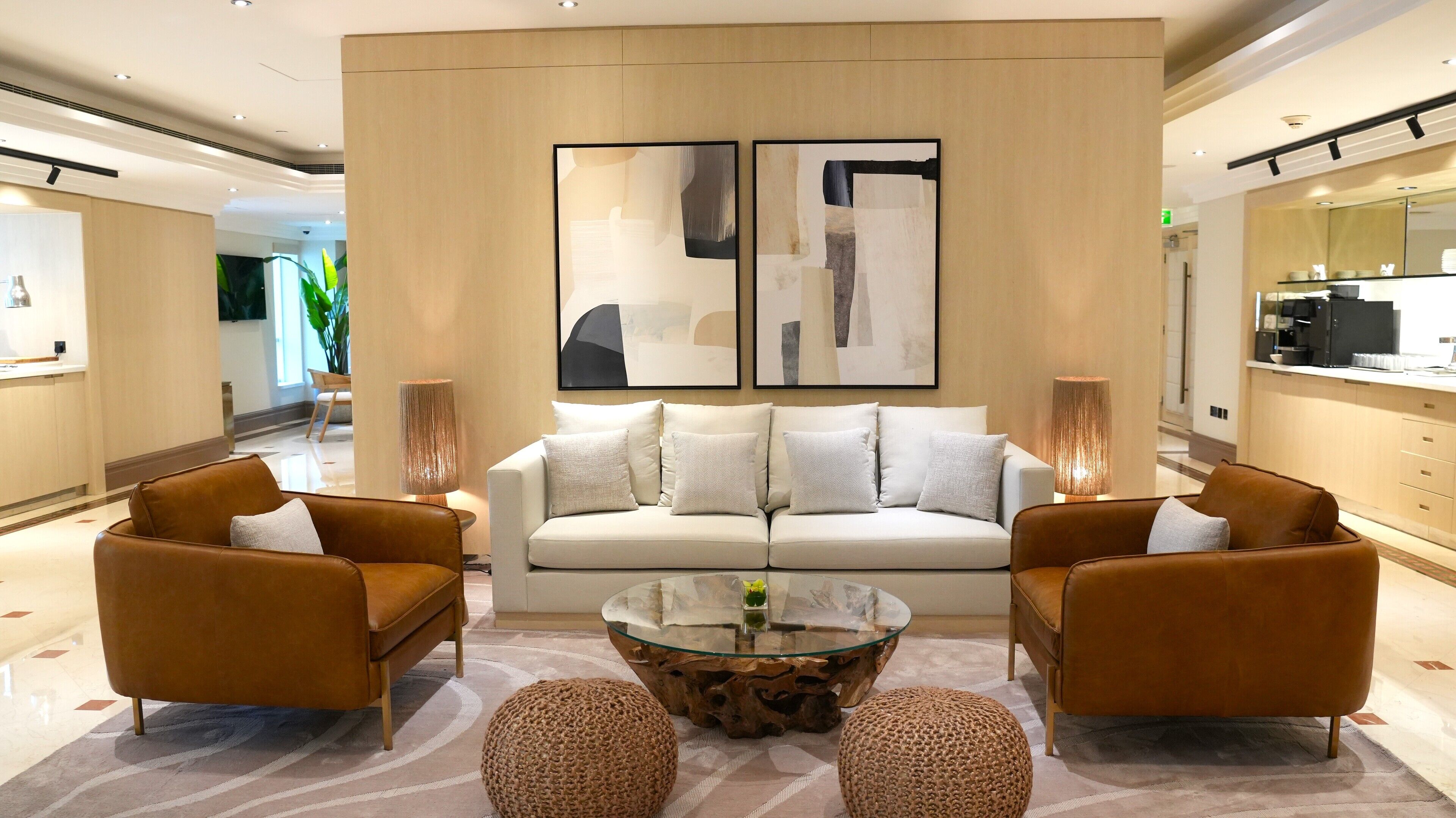 Een moderne hotel lobby met een zithoek, twee fauteuils, een glazen salontafel en een groot abstract schilderij boven de bank.