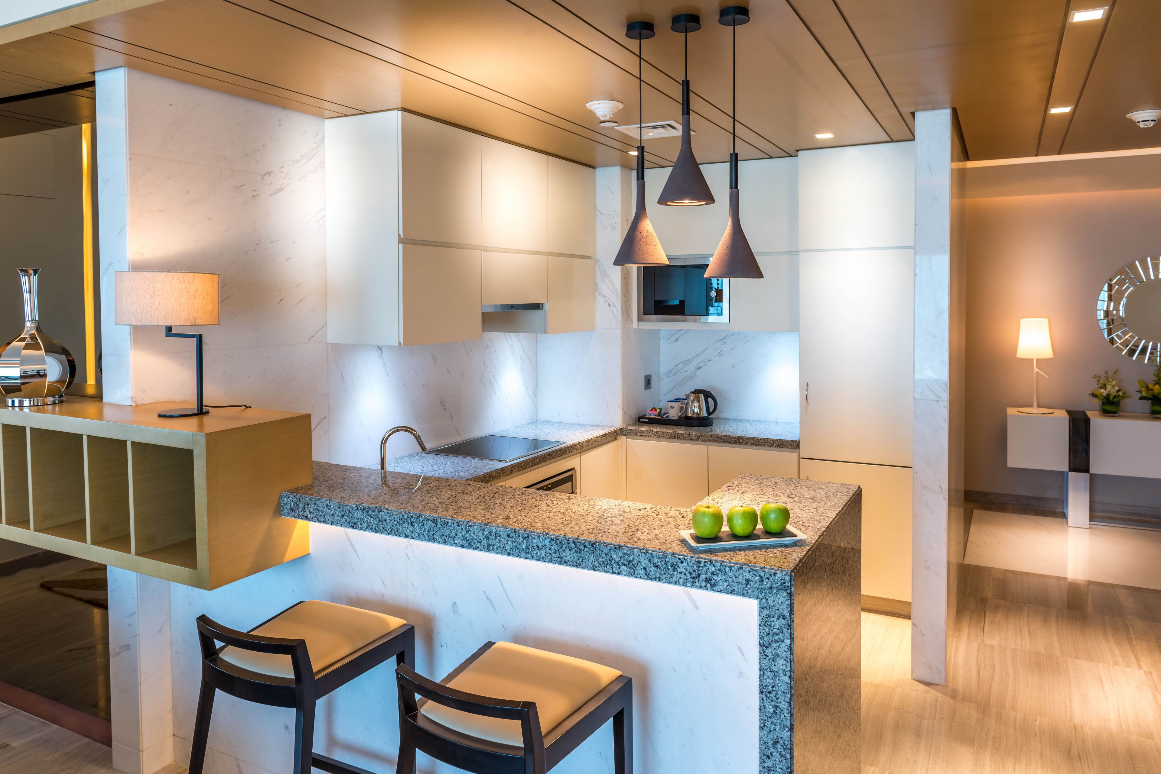 Une cuisine moderne dotée d’un îlot central, de tabourets de bar, de luminaires suspendus et d’un pare-feu en marbre.