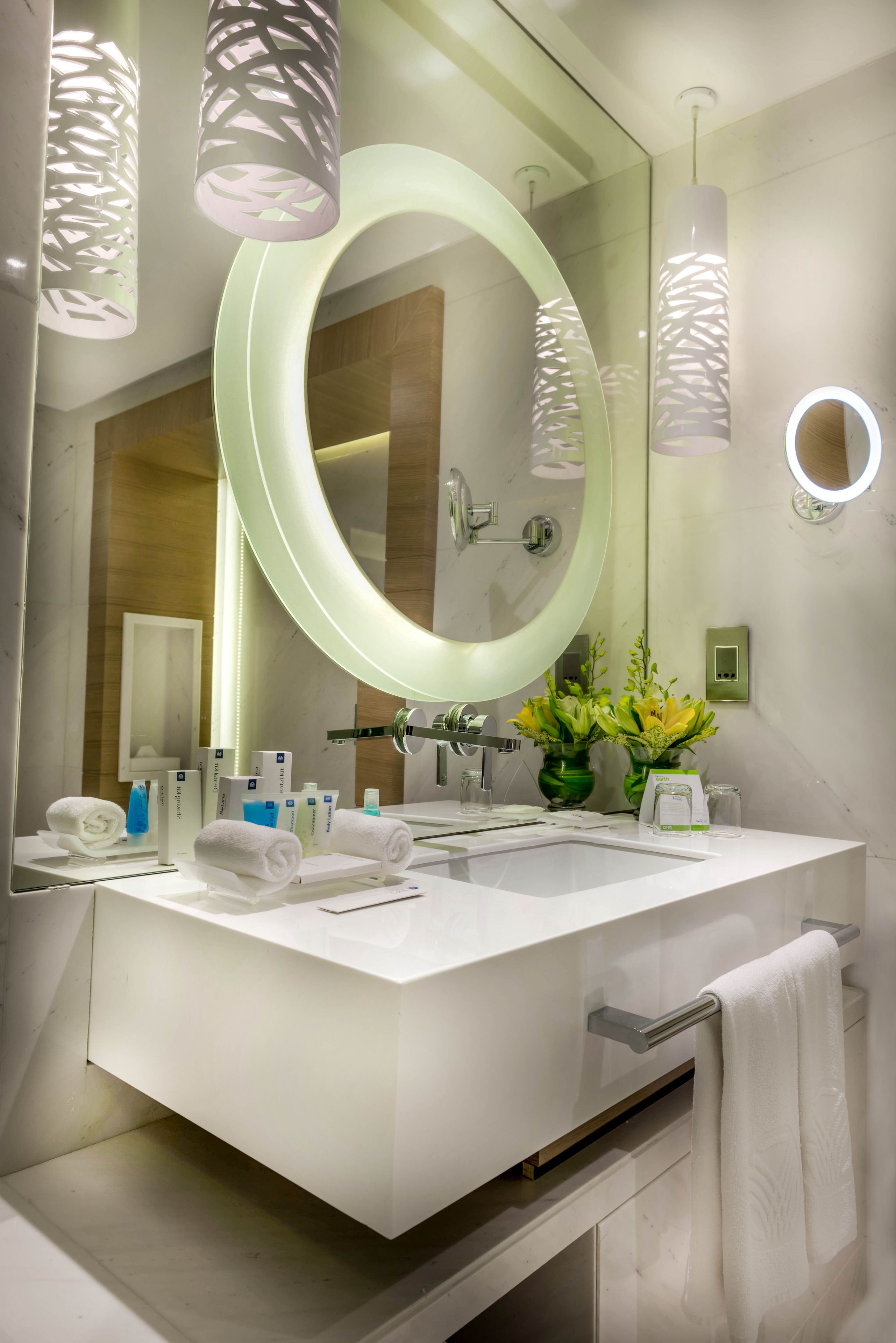 A modern bathroom with a large mirror, white fixtures, and a vase of flowers.