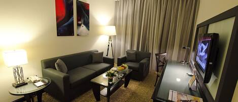 A hotel room with a sofa, armchairs, a coffee table, a TV, and a lamp.