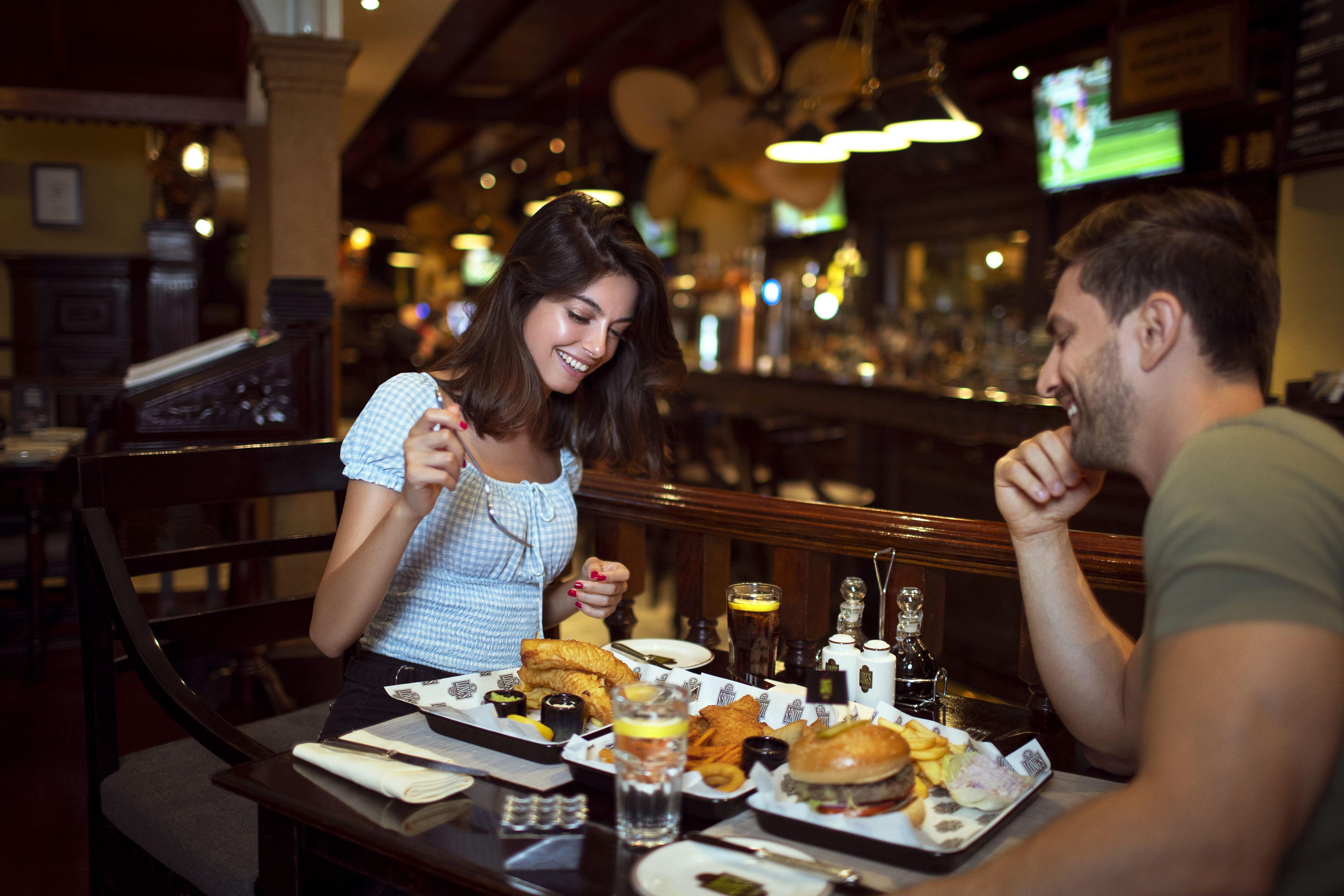 A restaurant interior with wooden furniture, a bar area, and a television screen in the background.
