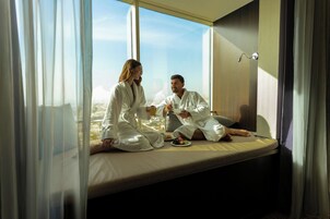 A couple in a hotel room with a large window, sitting on a bed with a view of the city.