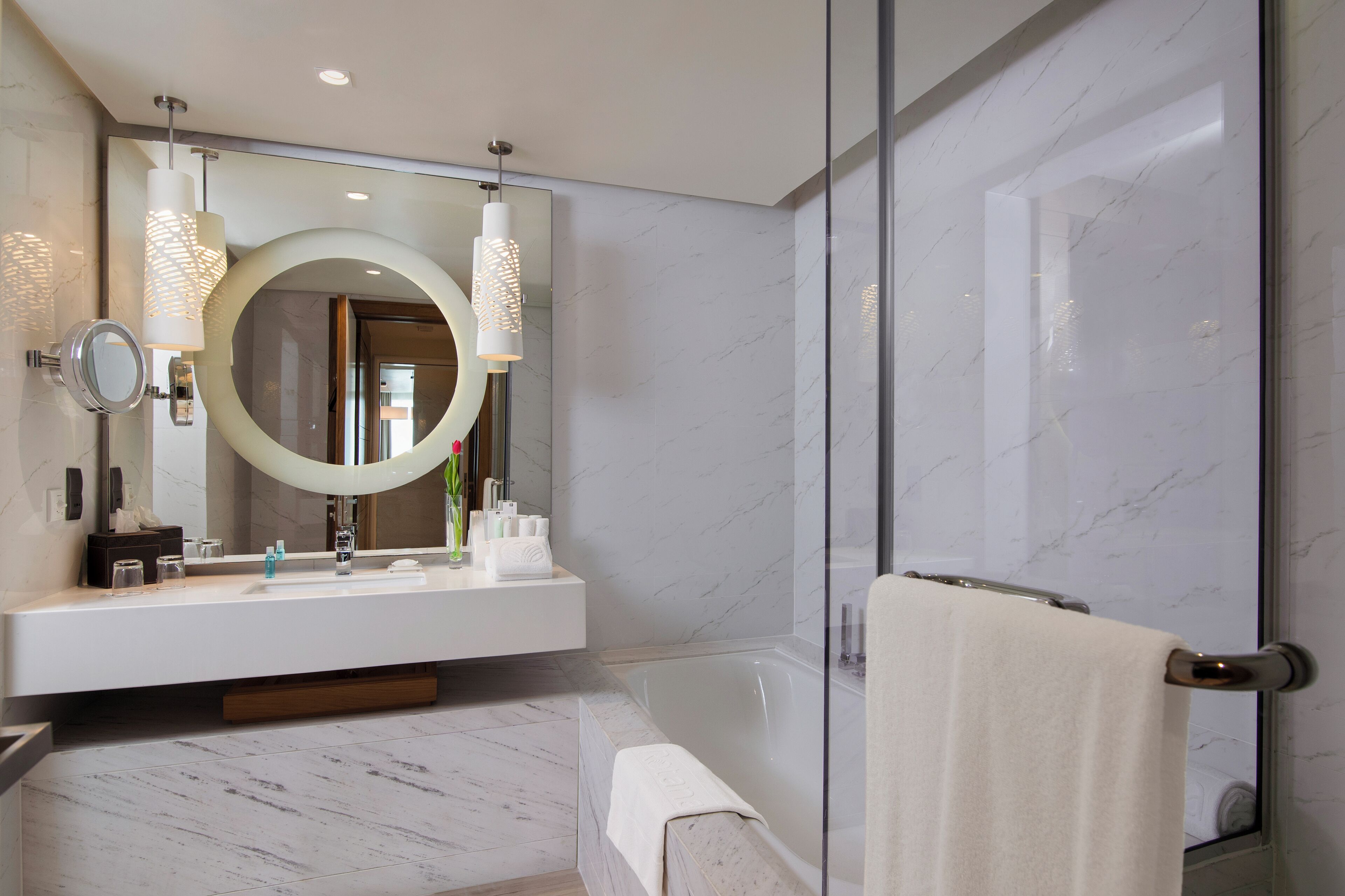 A modern bathroom with a large mirror, two pendant lights, a bathtub, and a glass shower enclosure.