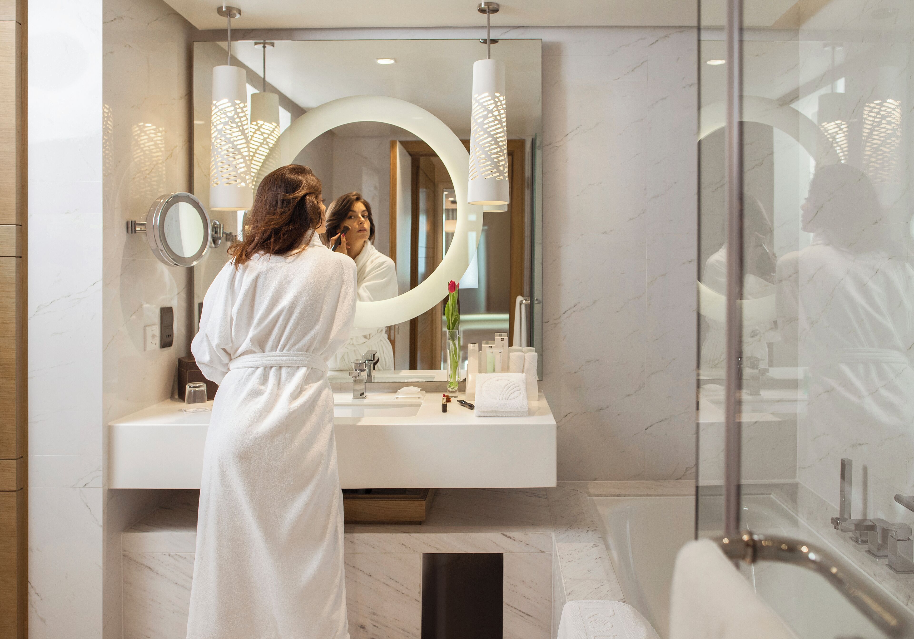 A modern bathroom with a large mirror, a round mirror, a white vanity, and a glass shower enclosure.
