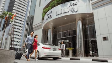 Guests can enter the hotel through the glass door, surrounded by a curved facade and large windows.