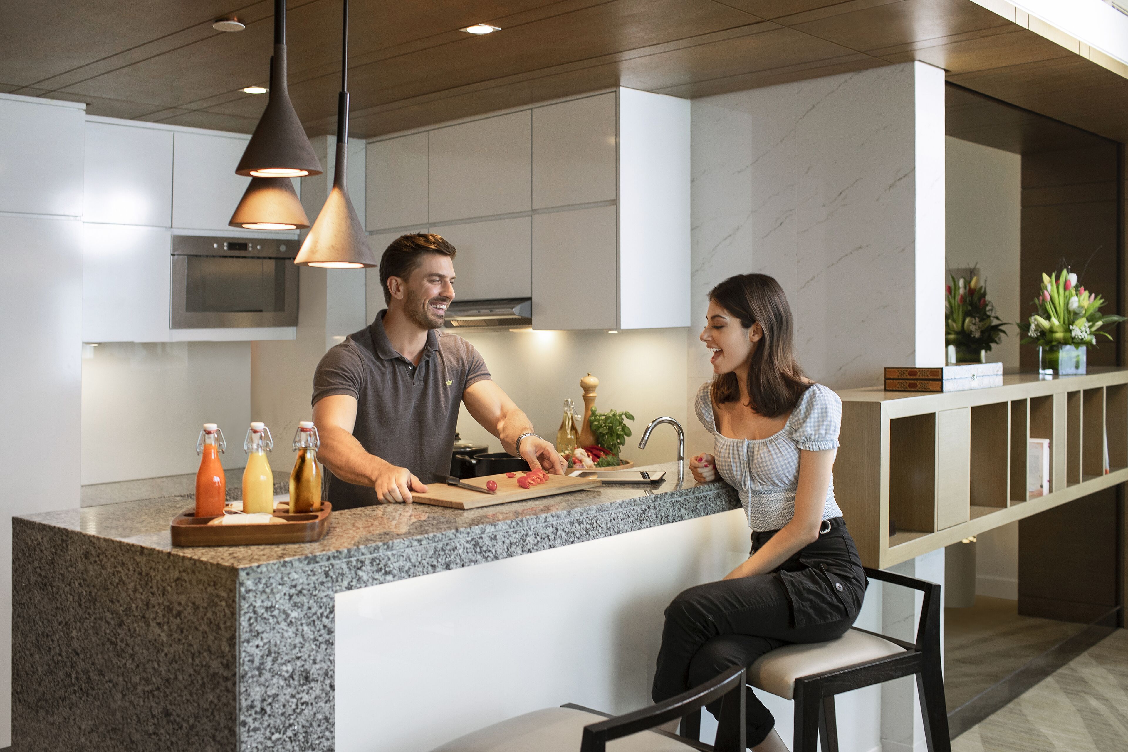 A modern kitchen with a granite countertop, stainless steel appliances, pendant lighting, and a seating area with a bench.