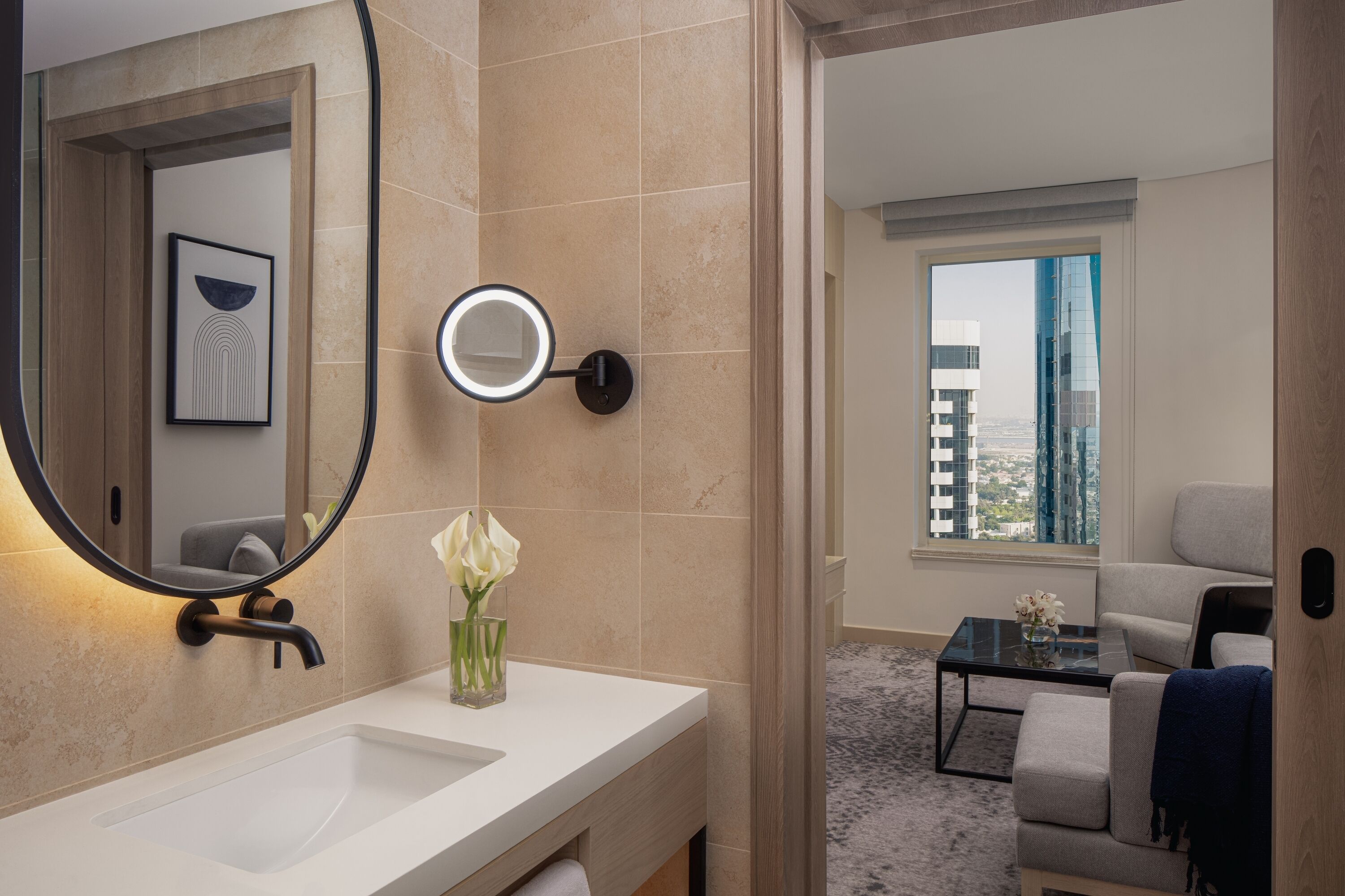 A modern bathroom with a large mirror, a round light, and a vase with flowers.
