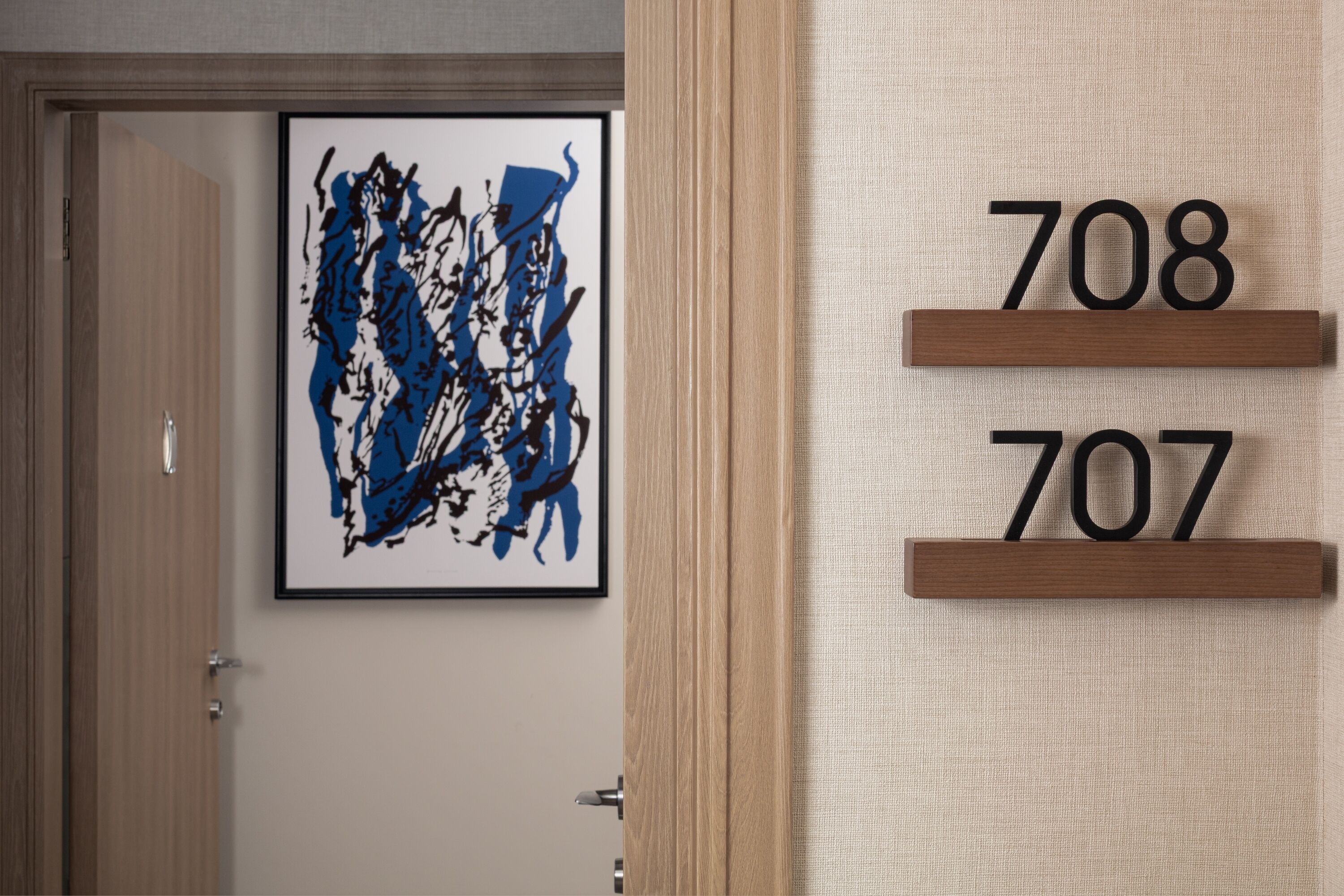 A door with a framed abstract painting and a wooden number display showing 708 and 707.
