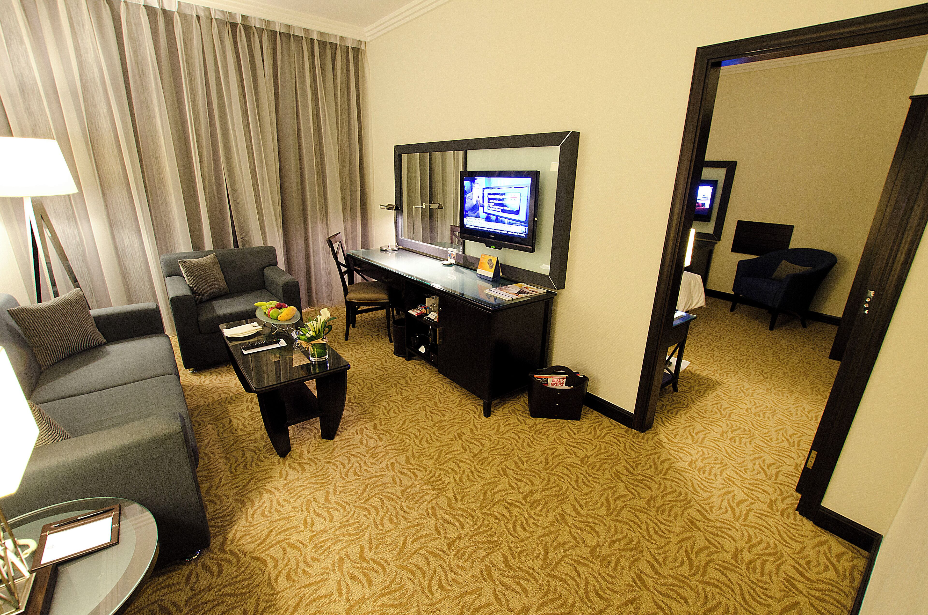 Una habitación de hotel con sofá, escritorio, ordenador, lámpara y espejo.