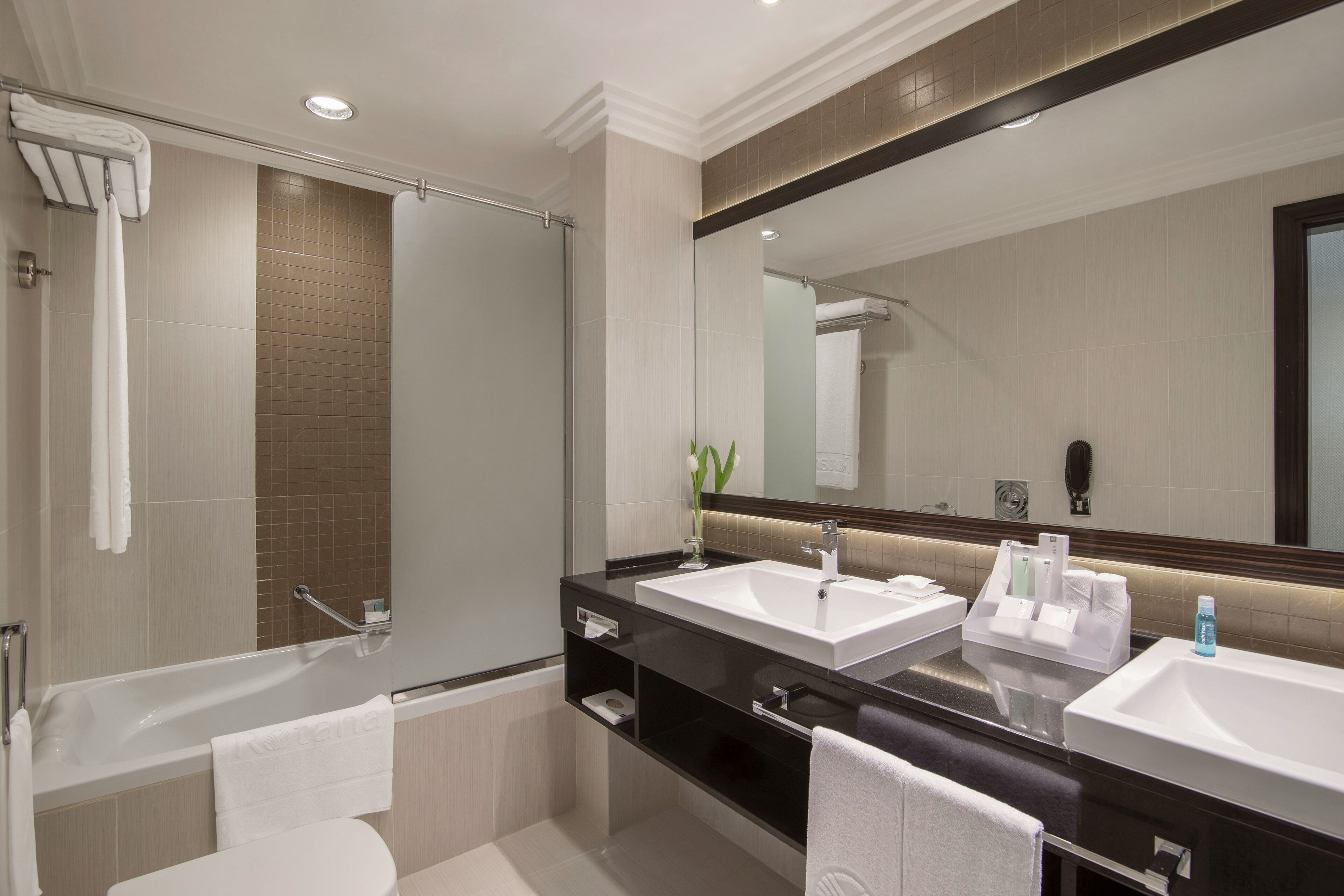 A modern bathroom with a bathtub, two sinks, a large mirror, and a shower.
