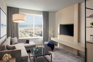 A modern living room with a large window, a sofa, a coffee table, a TV, and a bookshelf.