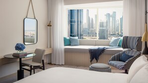 A modern hotel room with a large bed, a seating area with a view of the city skyline, a small table with books, and a lamp. - Towers Rotana (Dubai)