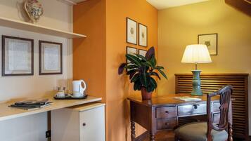 Une chambre d’hôtel équipée d’un bureau, d’une chaise, d’une lampe, d’une plante en pot et de tableaux encadrés accrochés au mur.