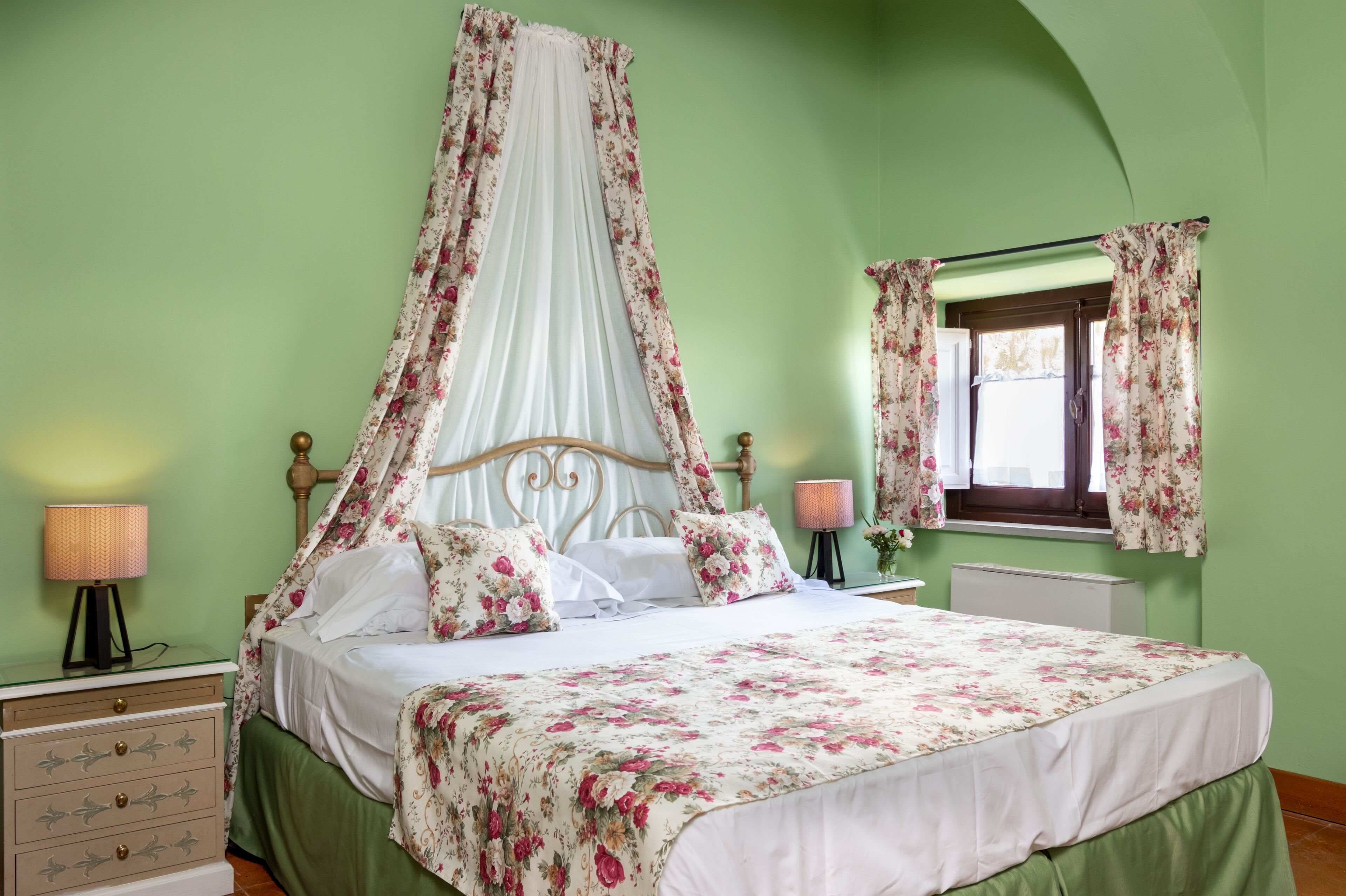 Ein Schlafzimmer mit Himmelbett, grünen Wänden und blumigem Bettzeug.