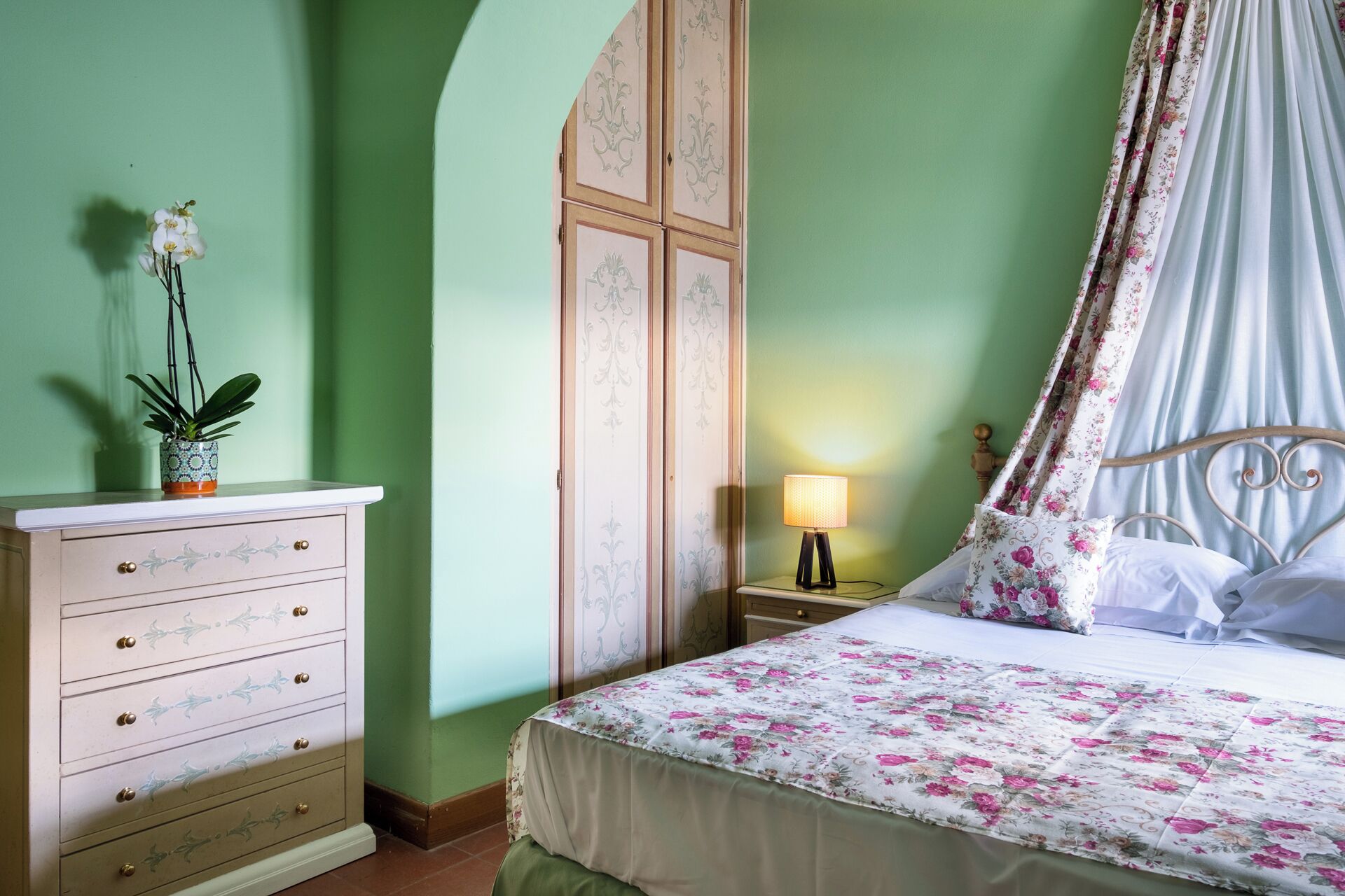 Un dormitorio con cama, mesita de noche, cómoda y dosel con estampado floral.