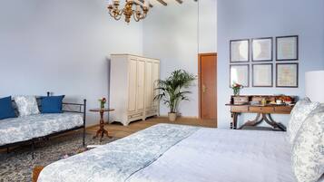 A bedroom with two beds, a wooden wardrobe, a desk with a chair, a chandelier, and framed documents on the wall.