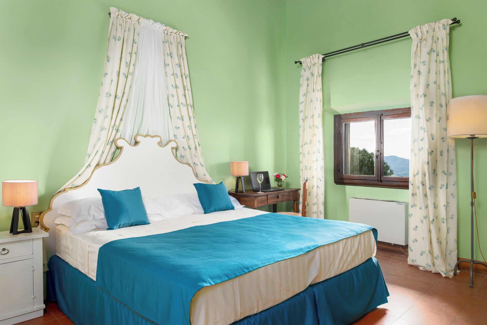 A bedroom with a bed, two bedside tables, a window, and a view of the outdoors.
