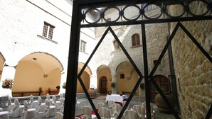 A courtyard with white chairs arranged in rows, a red carpet, and stone buildings with arches. - Villa Pitiana (Reggello)