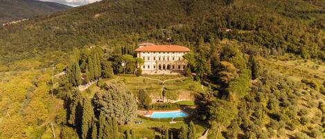 Un edificio grande e histórico rodeado de exuberantes jardines y una piscina.