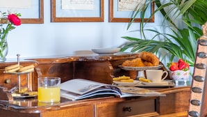 A wooden desk with a tray of croissants, a plate of strawberries, a glass of juice, and a vase with a red rose. - Villa Pitiana (Reggello)