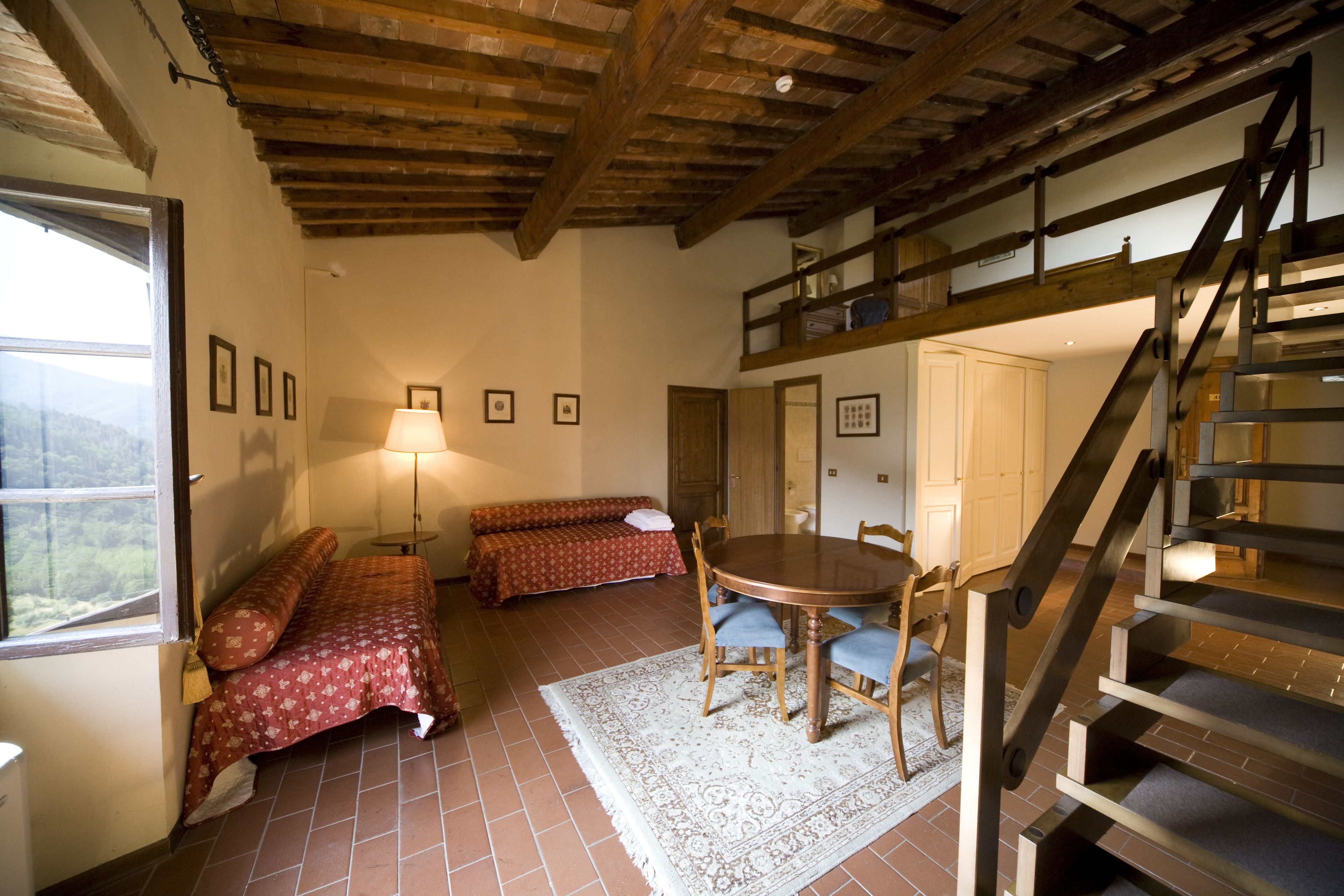 A cozy room with a wooden ceiling, a dining table with chairs, a sofa, and a staircase.