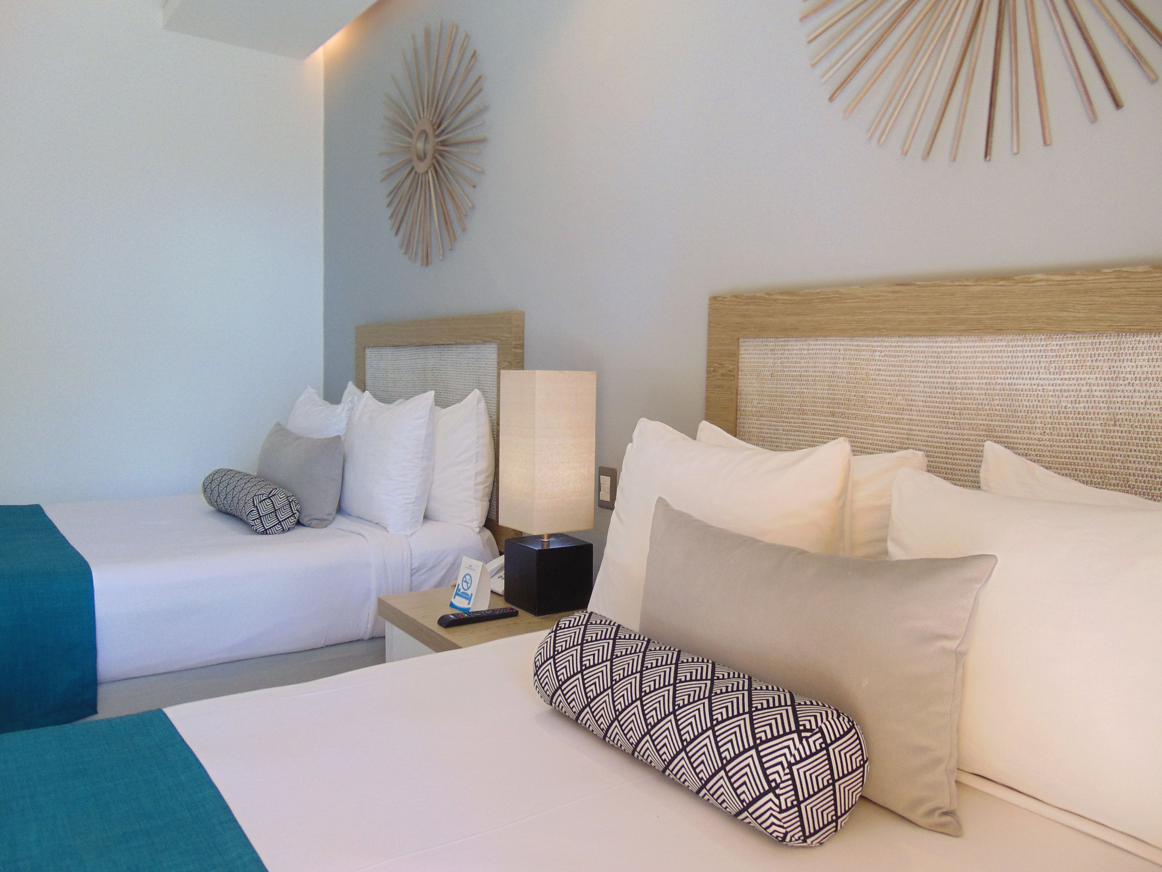 A hotel room with two beds, a nightstand with a lamp, and a decorative wall piece.