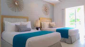 Hotelkamer met twee bedden, elk voorzien van witte lakens en een blauwgroene plaid. Er zijn decoratieve muurbevestigingen en een groot raam met uitzicht op groen.