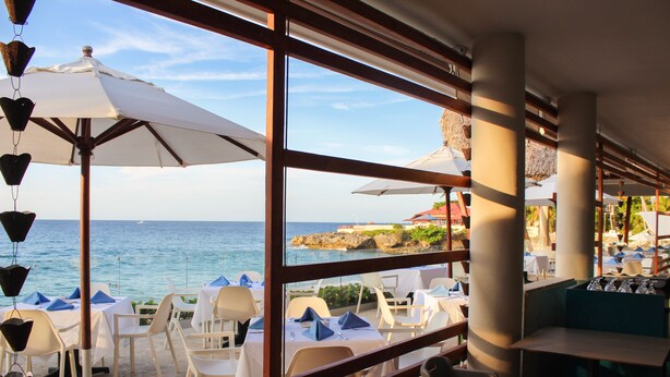 An outdoor dining area with tables and chairs, large umbrellas, and a view of the sea. - Casa Marina Sosua, Trademark by Wyndham Resort (Sosúa)