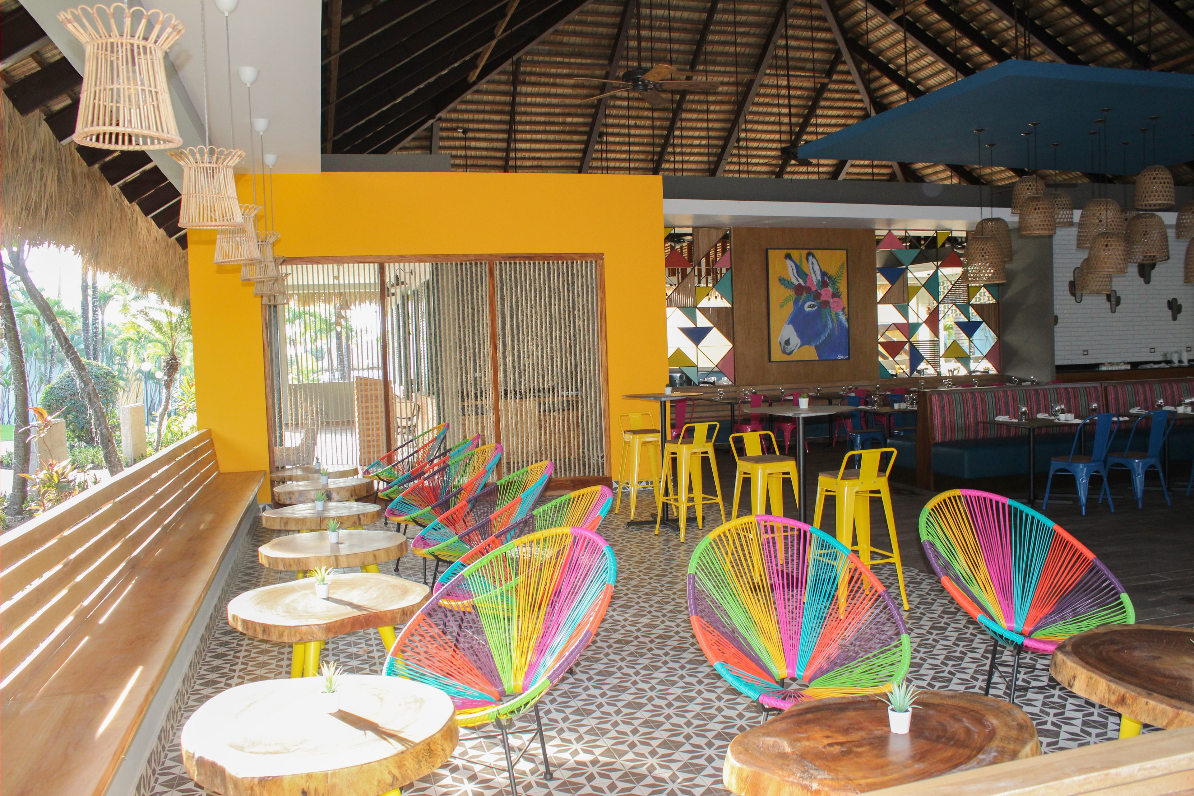 A restaurant with colorful chairs, wooden tables, and a yellow wall.