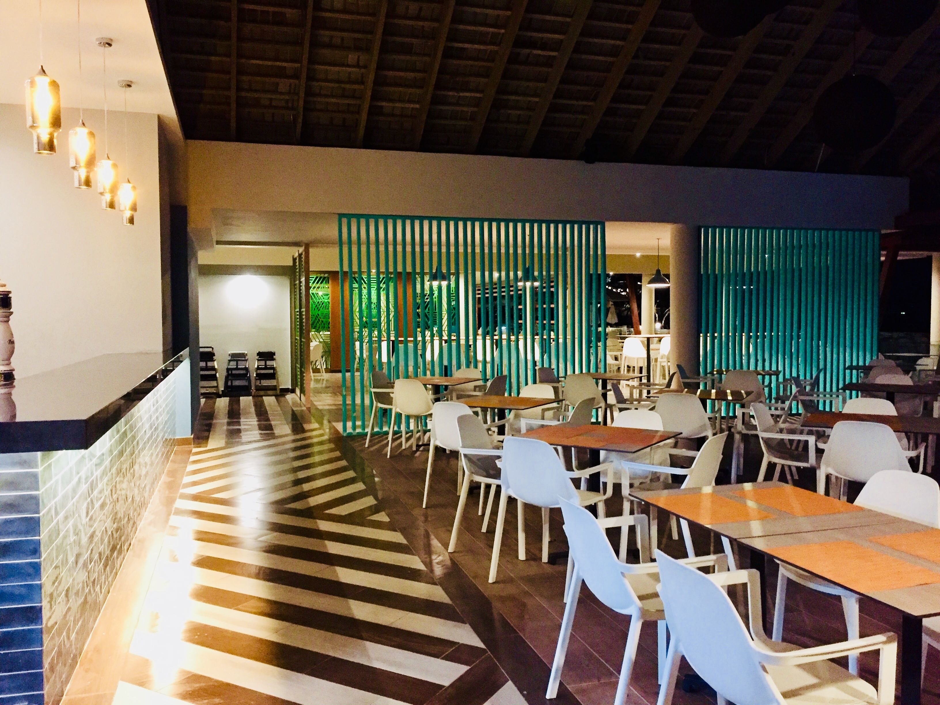 A restaurant with a modern interior, featuring striped flooring, white chairs, and a counter with a bar.