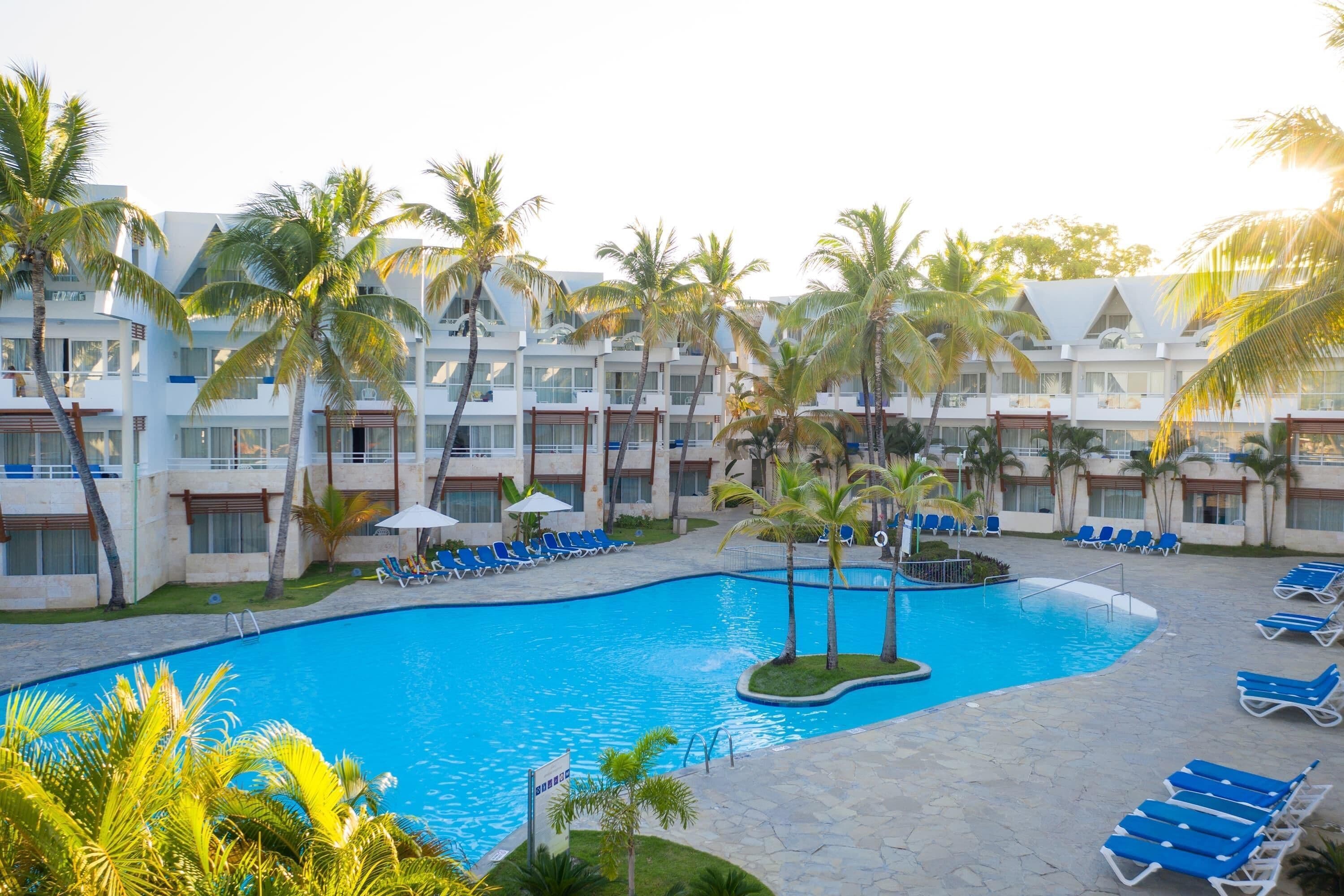 A resort with a swimming pool surrounded by palm trees and lounge chairs.