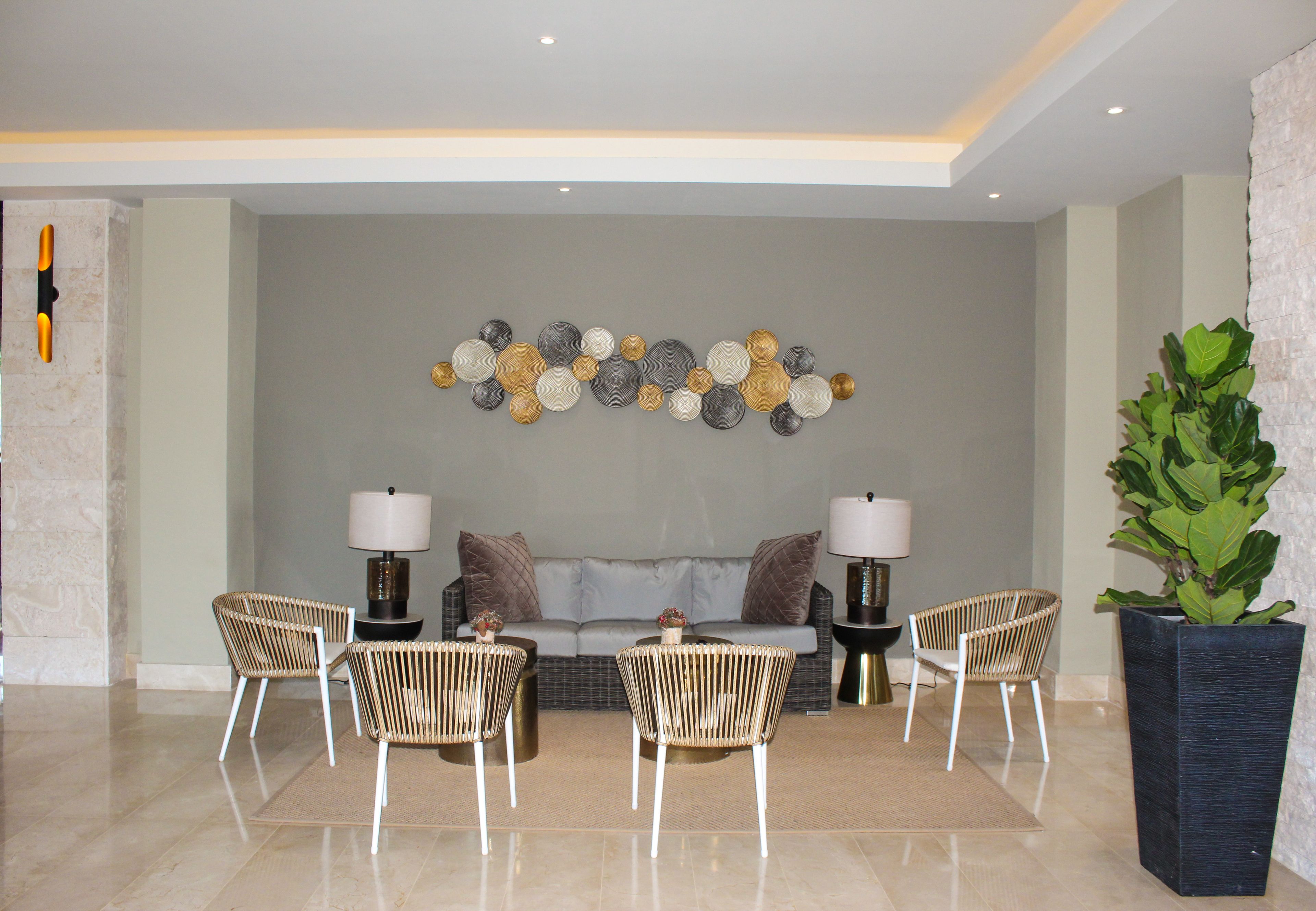 Ett modernt vardagsrum med en grå soffa, fyra fåtöljer i rotting, två sidobord med lampor och en dekorativ väggdekoration.