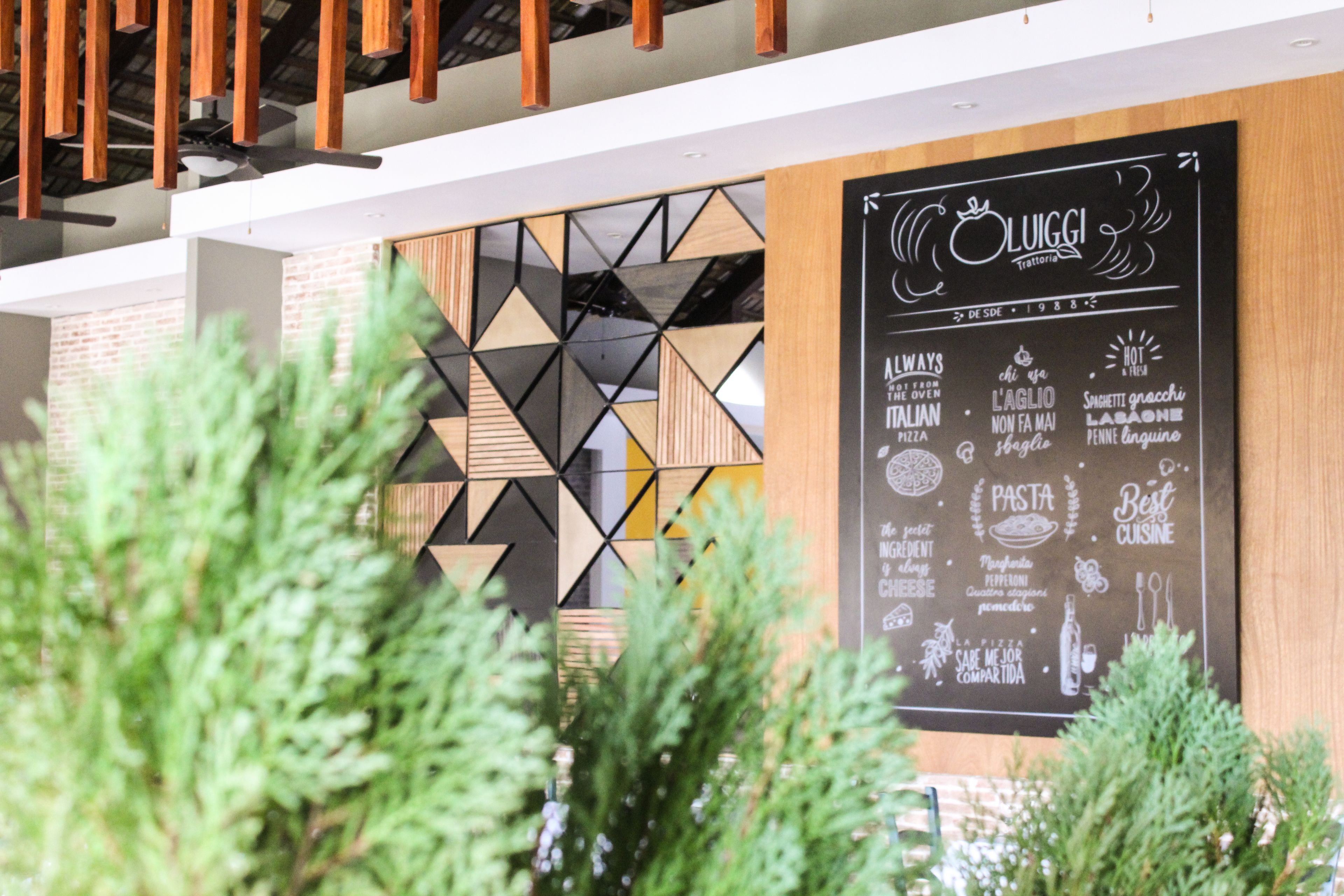 A restaurant interior with a chalkboard menu, geometric wall design, and wooden ceiling beams.