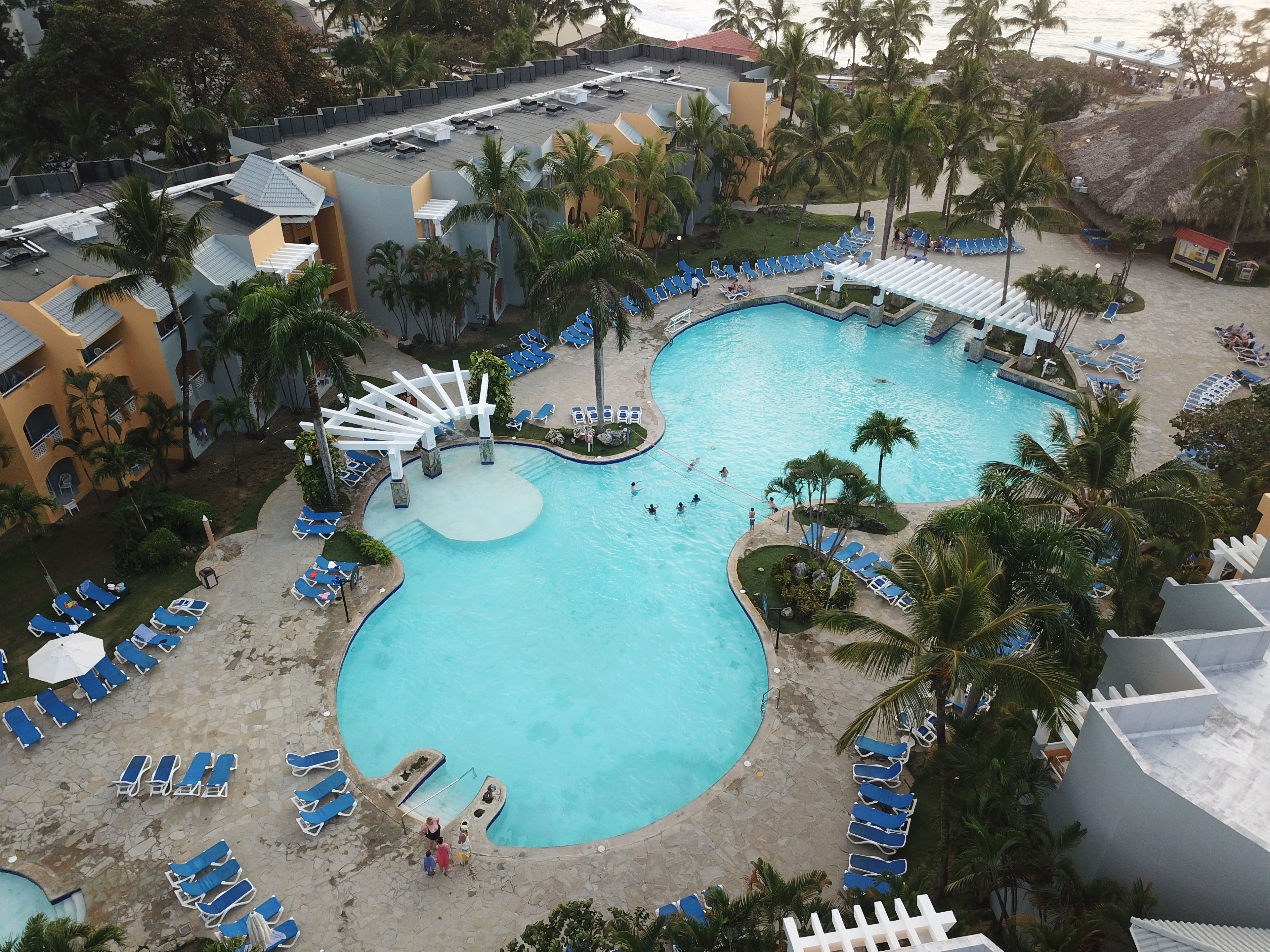 A resort pool area with multiple swimming pools, lounge chairs, and palm trees.