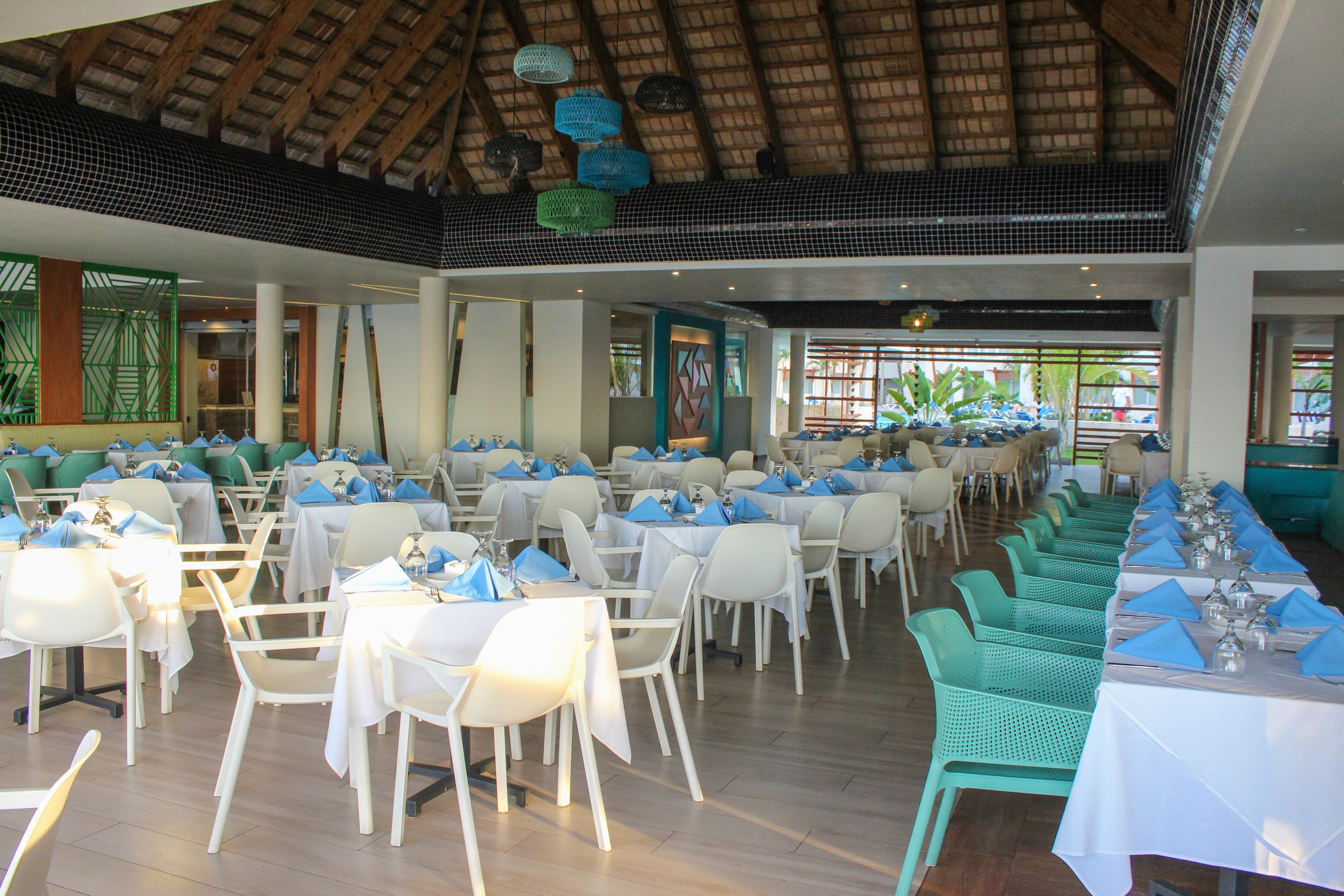 A restaurant with multiple tables and chairs, a thatched roof ceiling, and a view of the outdoors.