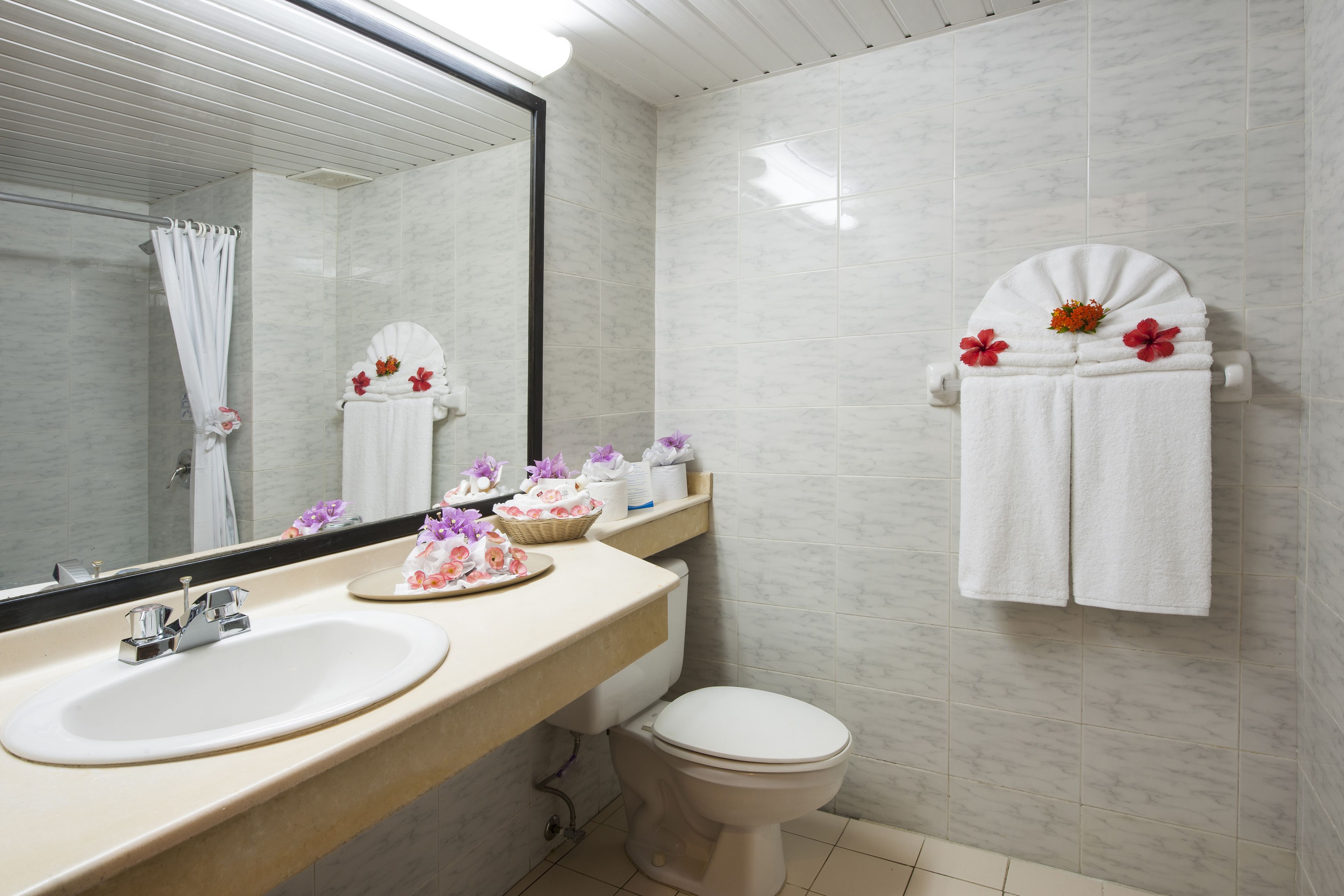 A bathroom with a sink, toilet, and mirror. There are towels and flowers on the wall.