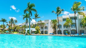 A resort pool with clear blue water, surrounded by palm trees and a white building with balconies. - Casa Marina Sosua, Trademark by Wyndham Resort (Sosúa)