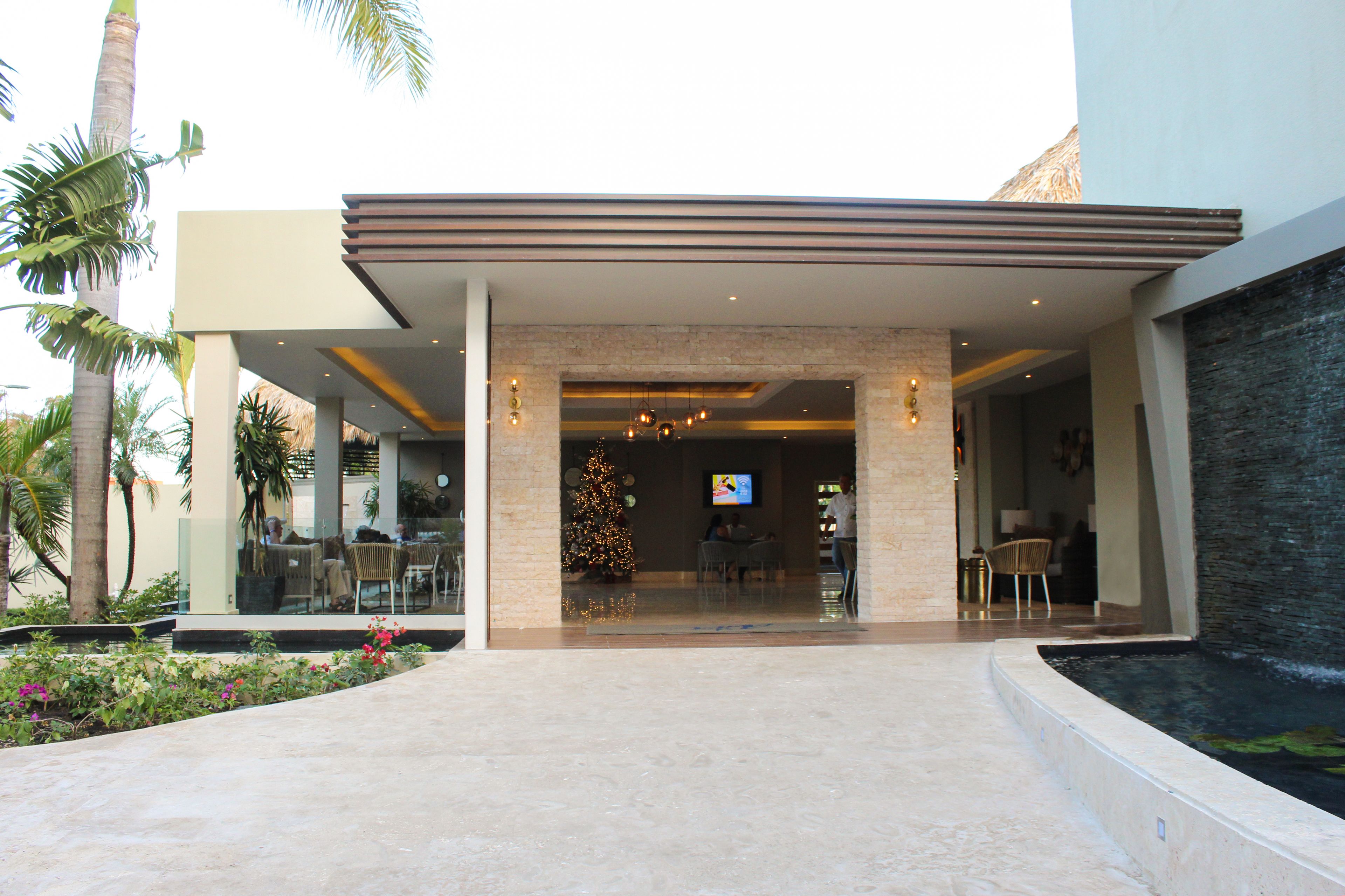 Entrada de hotel moderna com fachada de vidro, uma árvore de Natal e área de estar ao ar livre.