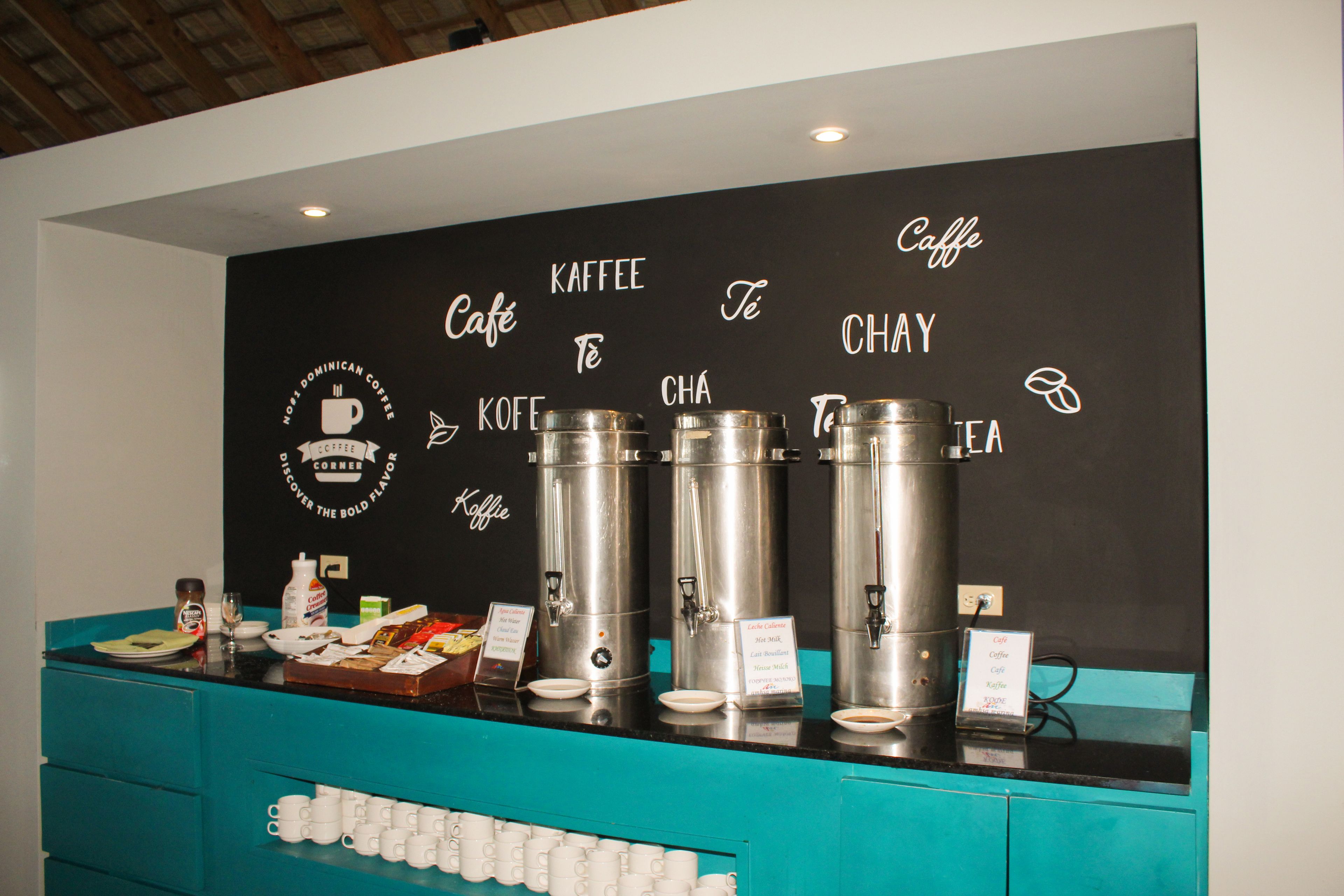 Una estación de café con varios dispensadores y un cartel que indica los tipos de bebidas disponibles.