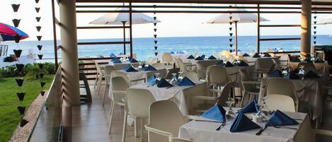 Un restaurant dont les tables sont dressées pour le dîner, avec vue sur l’océan.