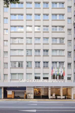 A multi-story hotel with a modern facade, a ground-level entrance, and flags at the top. - Savoy Othon Lite (Rio de Janeiro)