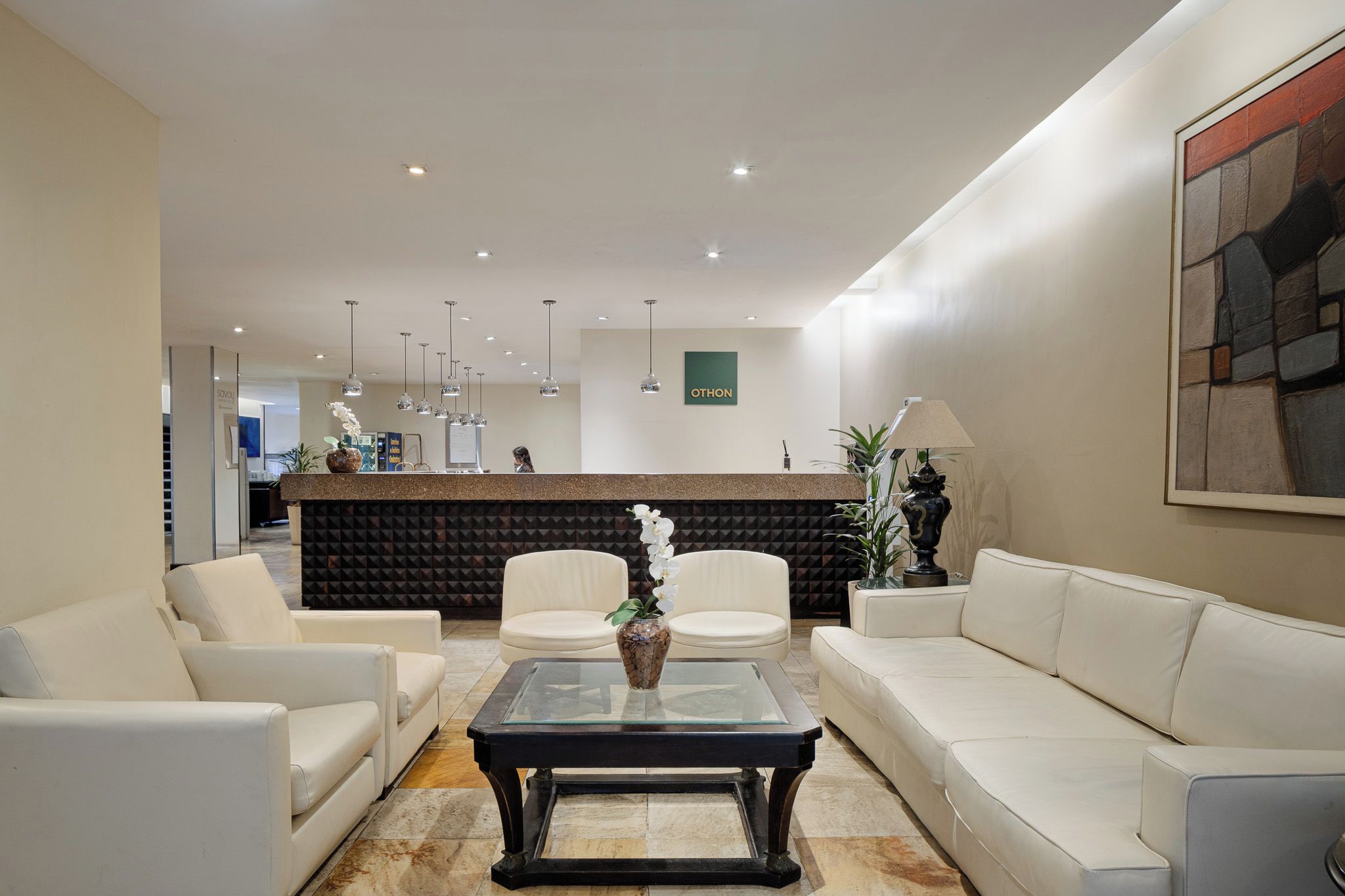 A reception area with a counter, white sofas, a glass coffee table, and pendant lighting.