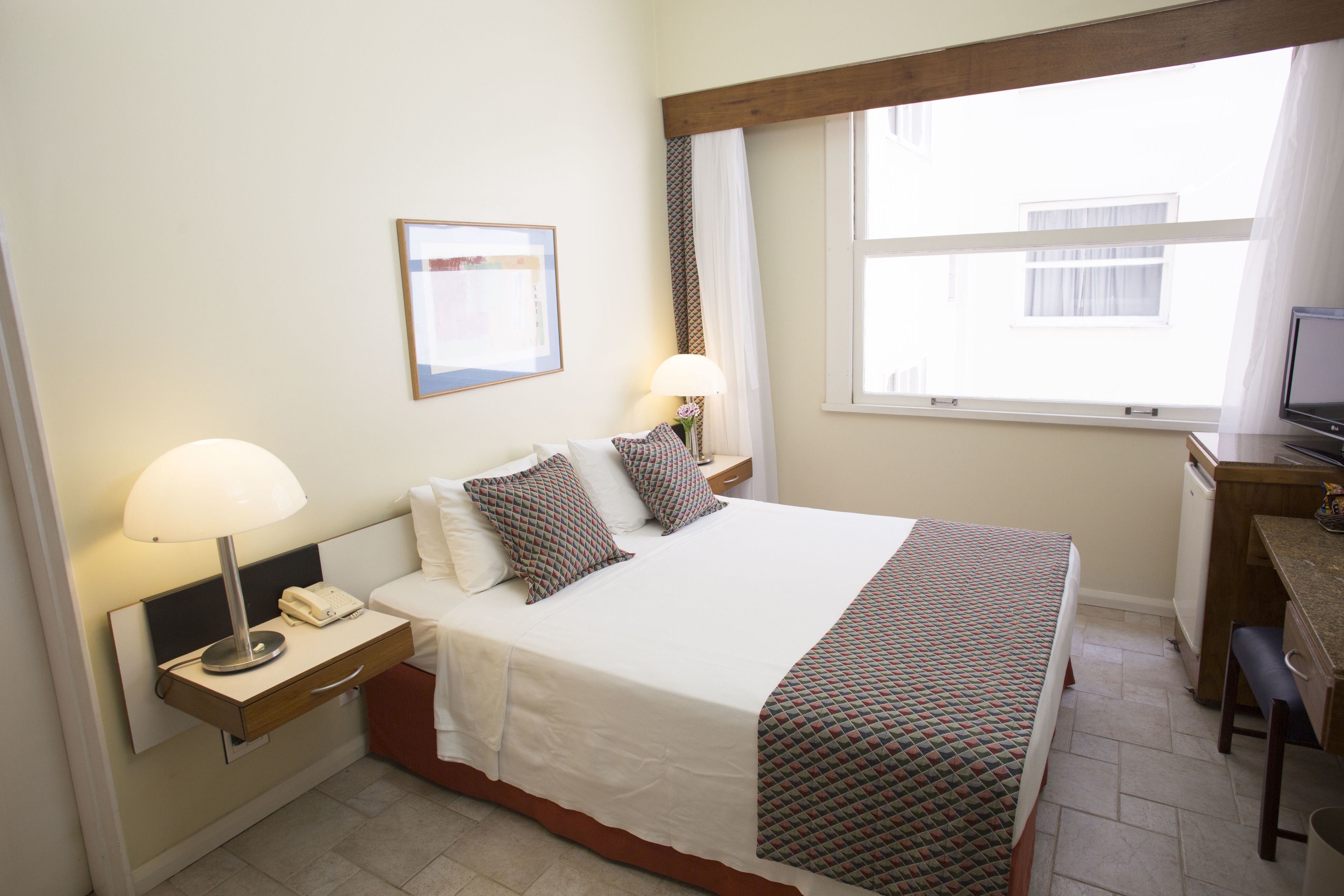 A neatly arranged hotel room with a bed, bedside table, lamp, and a desk with a chair.